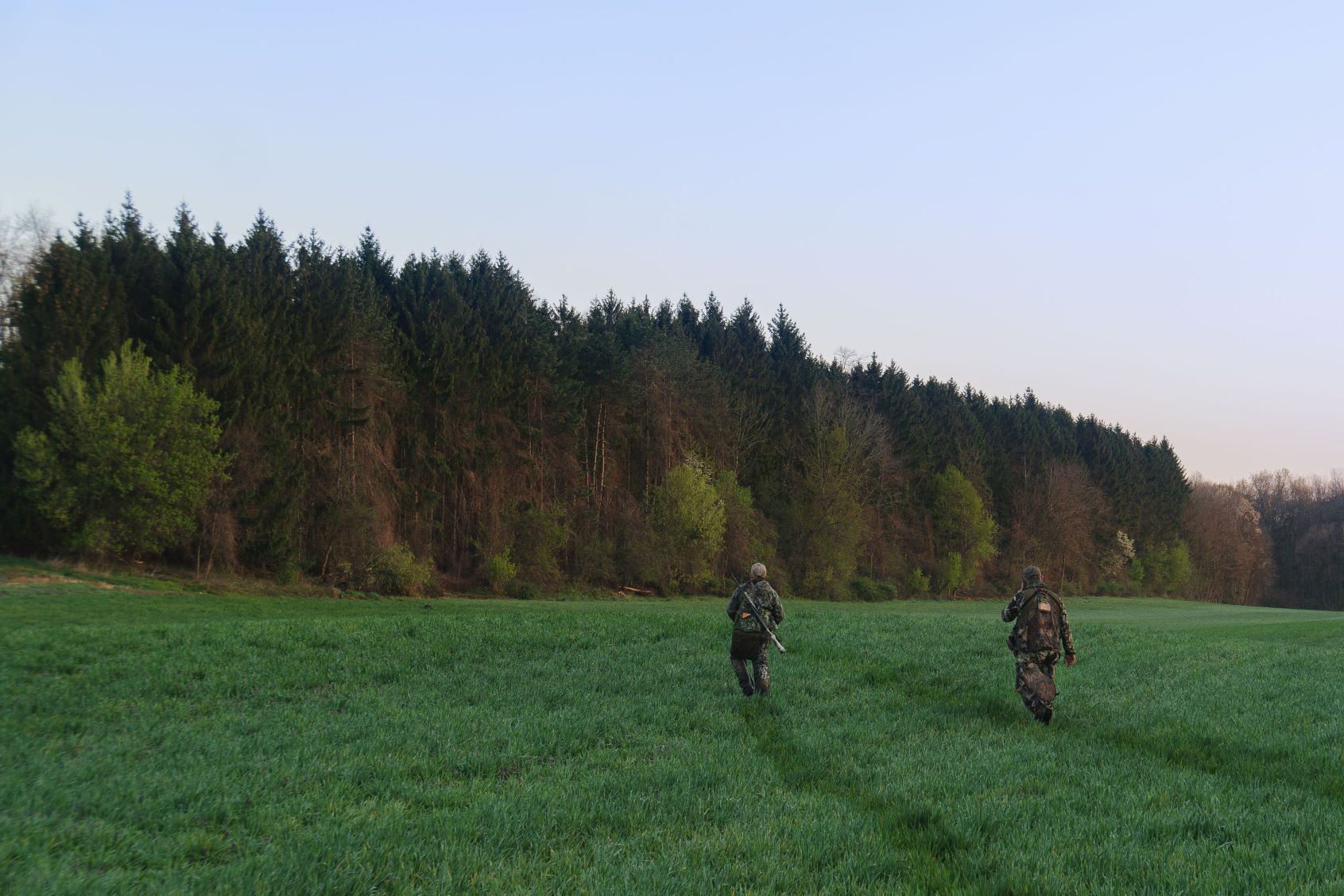 Youth hunter and mentor walking through grass field